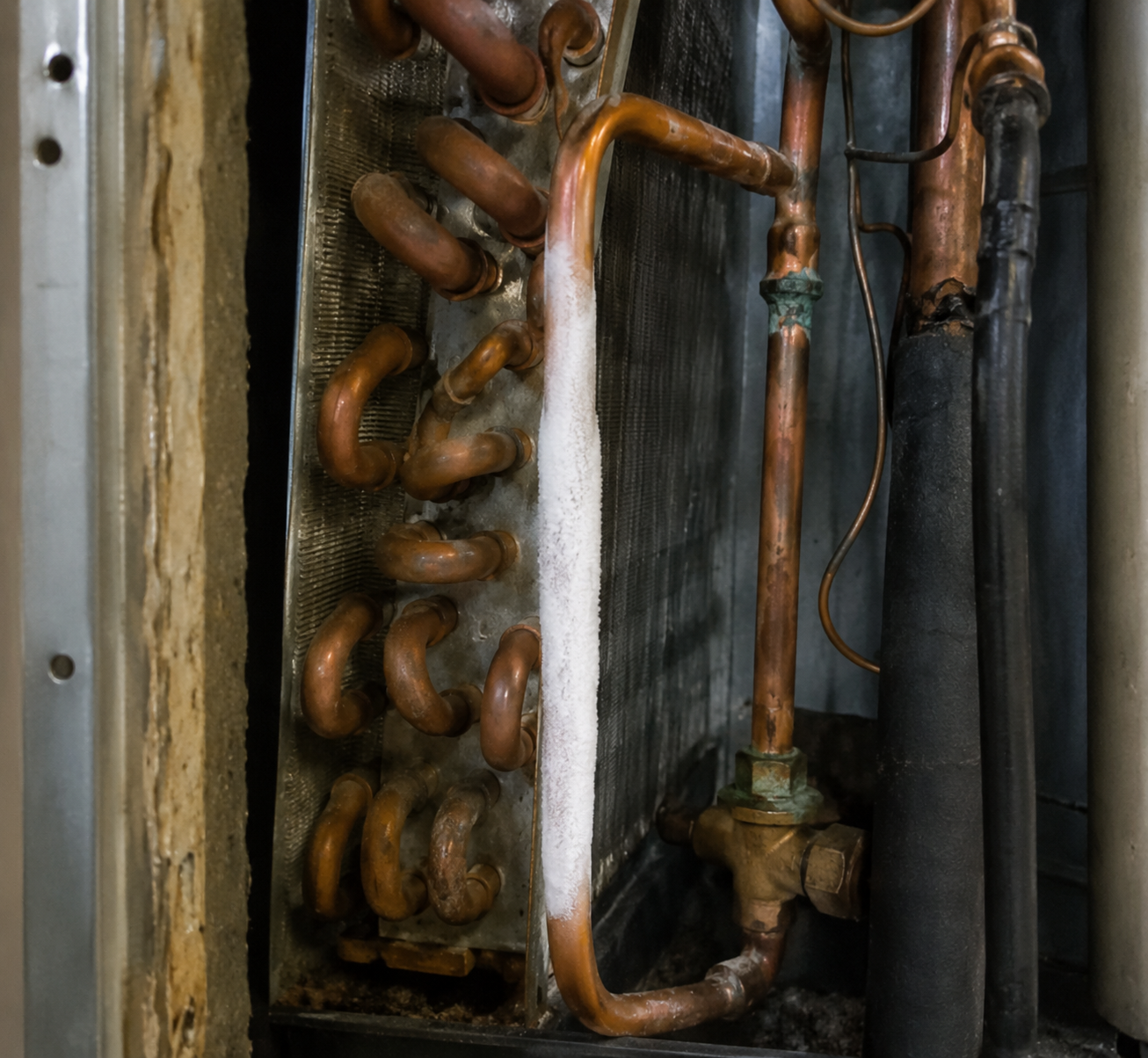 Close-up of an indoor AC evaporator coil with one copper refrigerant line covered in frost.